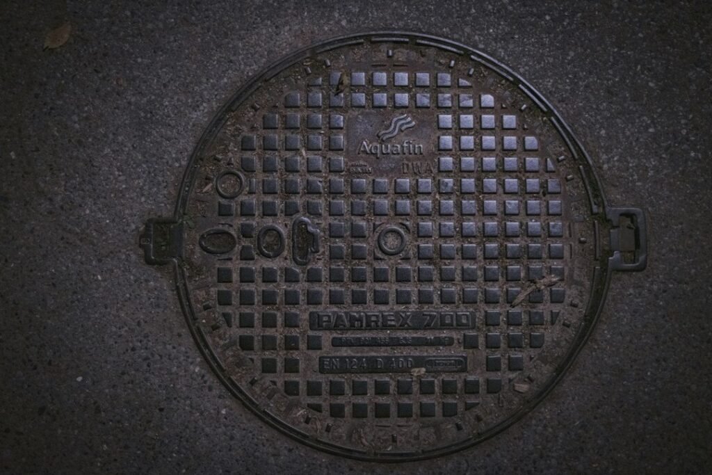Grey round drainage inspection cover set into paving beside a residential property